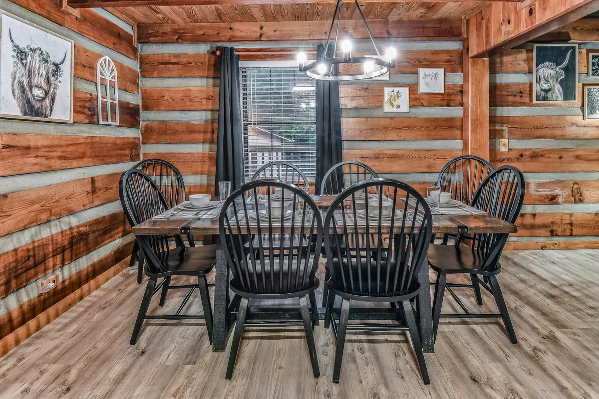 A warm and welcoming dining space with a large table and black chairs, surrounded by wooden walls and decorative wall art. The table is ready for family dinners, board games, or casual conversations.