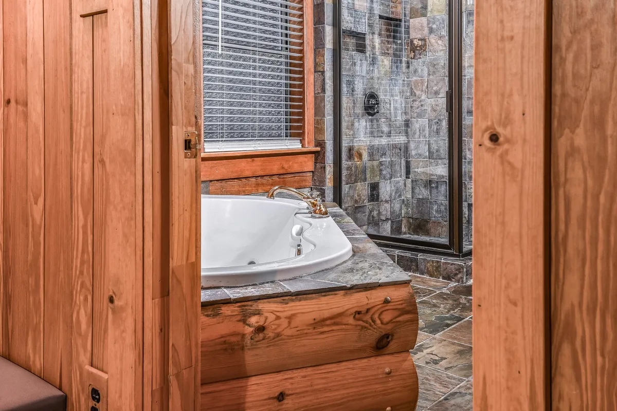 A bathroom oasis featuring a luxurious jacuzzi tub, a stone tile walk-in shower, and wood paneling that adds warmth. Gentle lighting makes the space feel serene and inviting, perfect for unwinding and self-care at the end of the day.