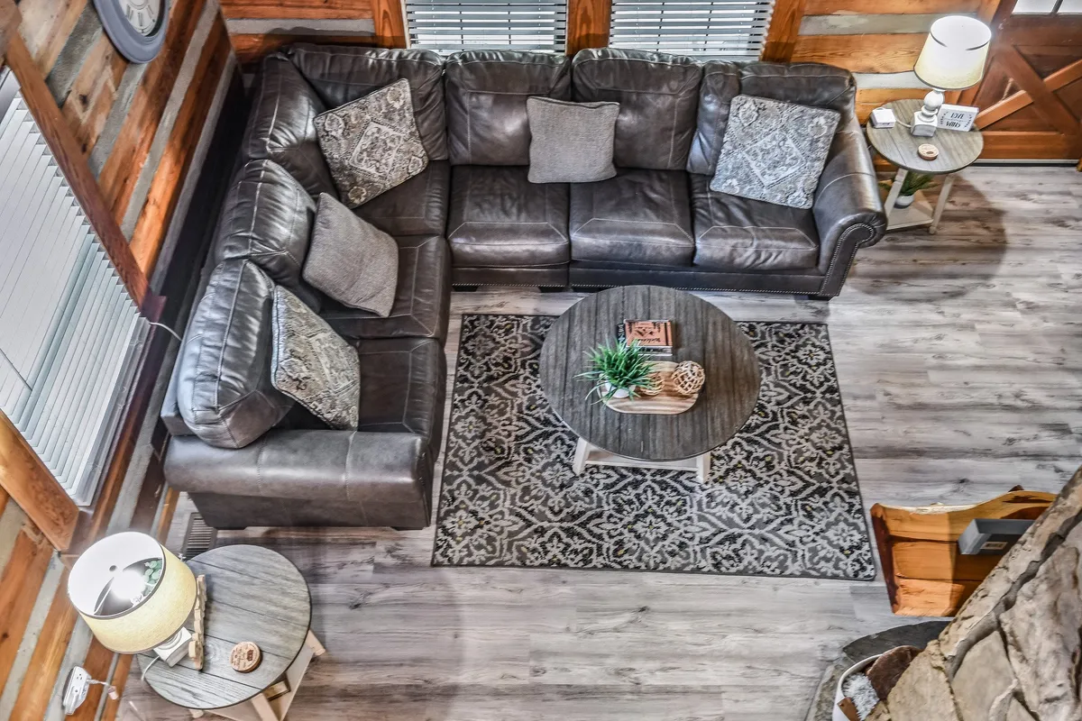 A large leather sectional sofa sits at the heart of this living room, complemented by a coffee table adorned with decorative items and an inviting area rug. Warm wooden accents and ample lighting contribute to a comfortable, welcoming atmosphere, ideal for relaxation and gatherings.