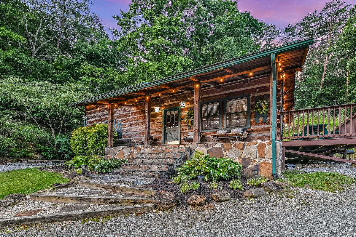 The log cabin’s front porch offers rustic stone steps, outdoor seating, and a view of lush mountain greenery. The setting feels serene and welcoming, inviting guests to relax, enjoy a meal, or watch the sunset from the deck.