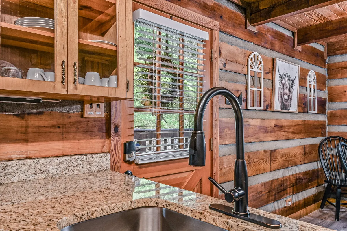 A bright, rustic kitchen with granite countertops and wooden cabinetry, filled with natural light from a nearby window. The scene suggests baking or cooking together, with ample space for guests to chat, snack, or help prepare meals, reinforcing the communal aspect.